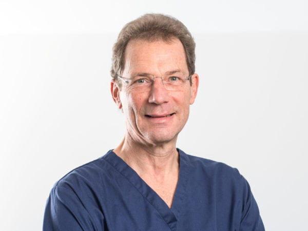 Picture of dr Keith Smith, Caucasian male with light brown hair and glasses wearing blue scrubs
